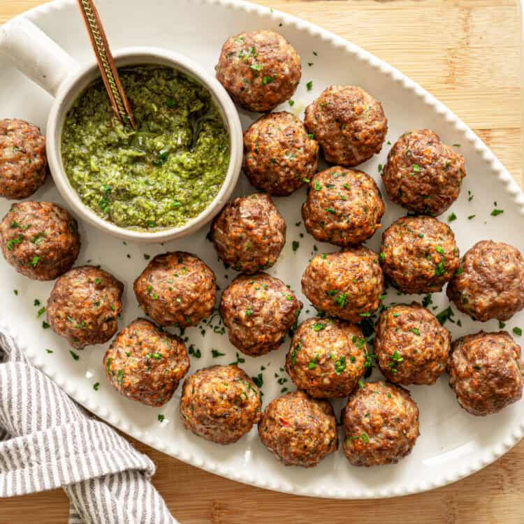 Baked healthy meatballs on a platter with pesto in a small bowl.