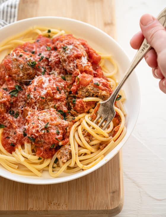 fork twirling spaghetti that is topped with Italian meatballs and sauce