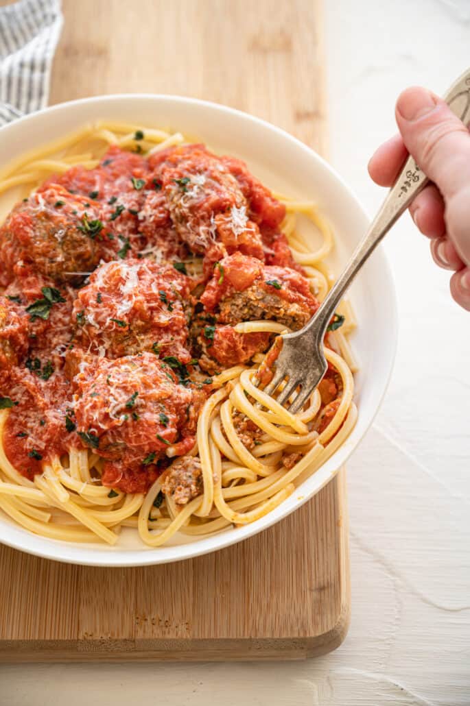 fork twirling spaghetti that is topped with Italian meatballs and sauce