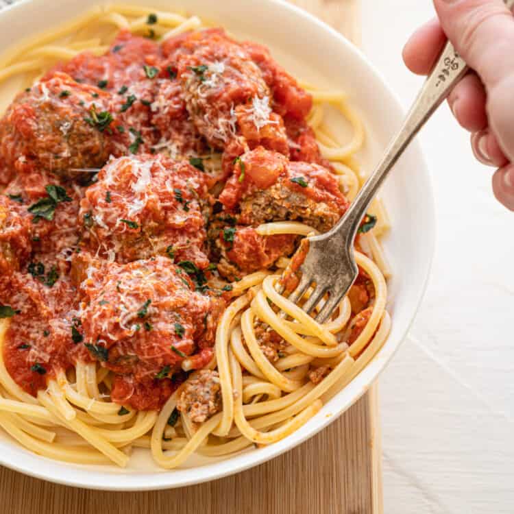 A fork twirling spaghetti that is topped with meatballs and marinara sauce.