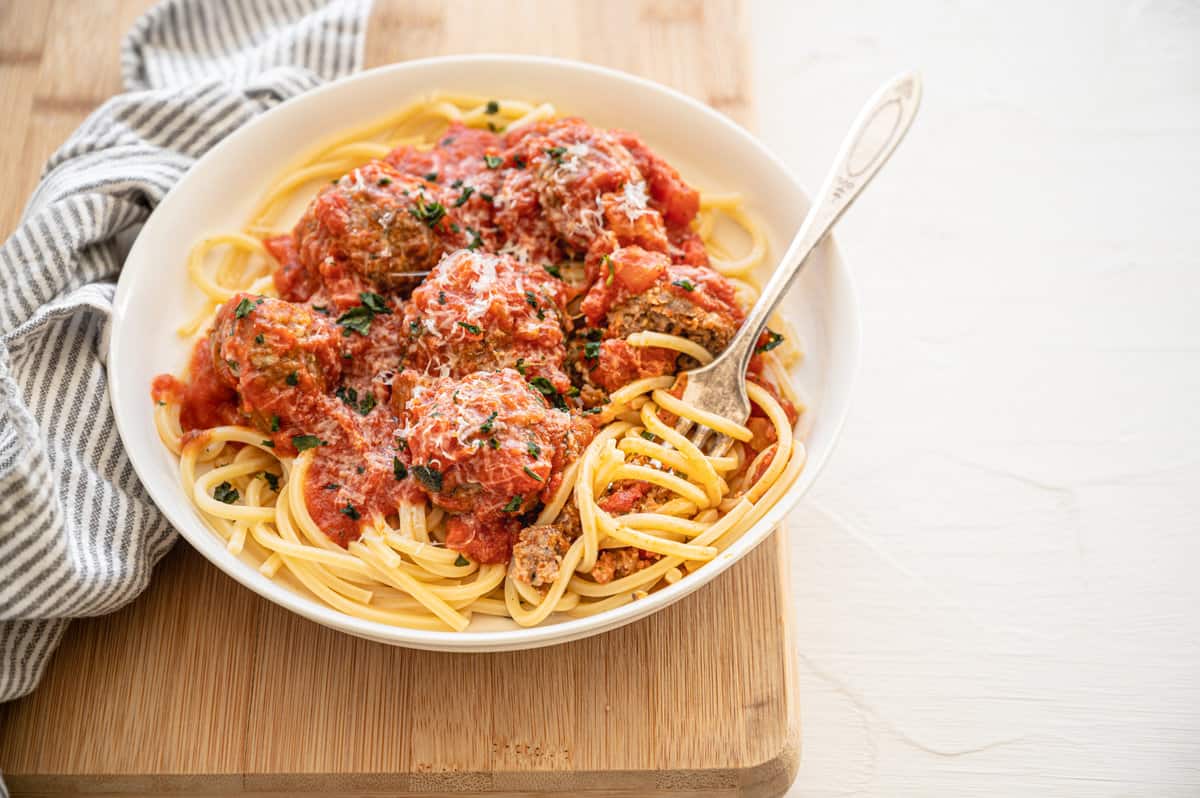 Fork twirling spaghetti that is topped with meatballs and sauce.