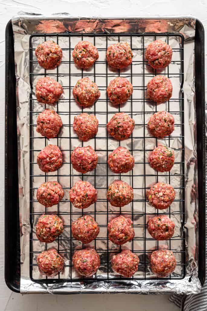 rolled meatballs on a rack over a baking sheet