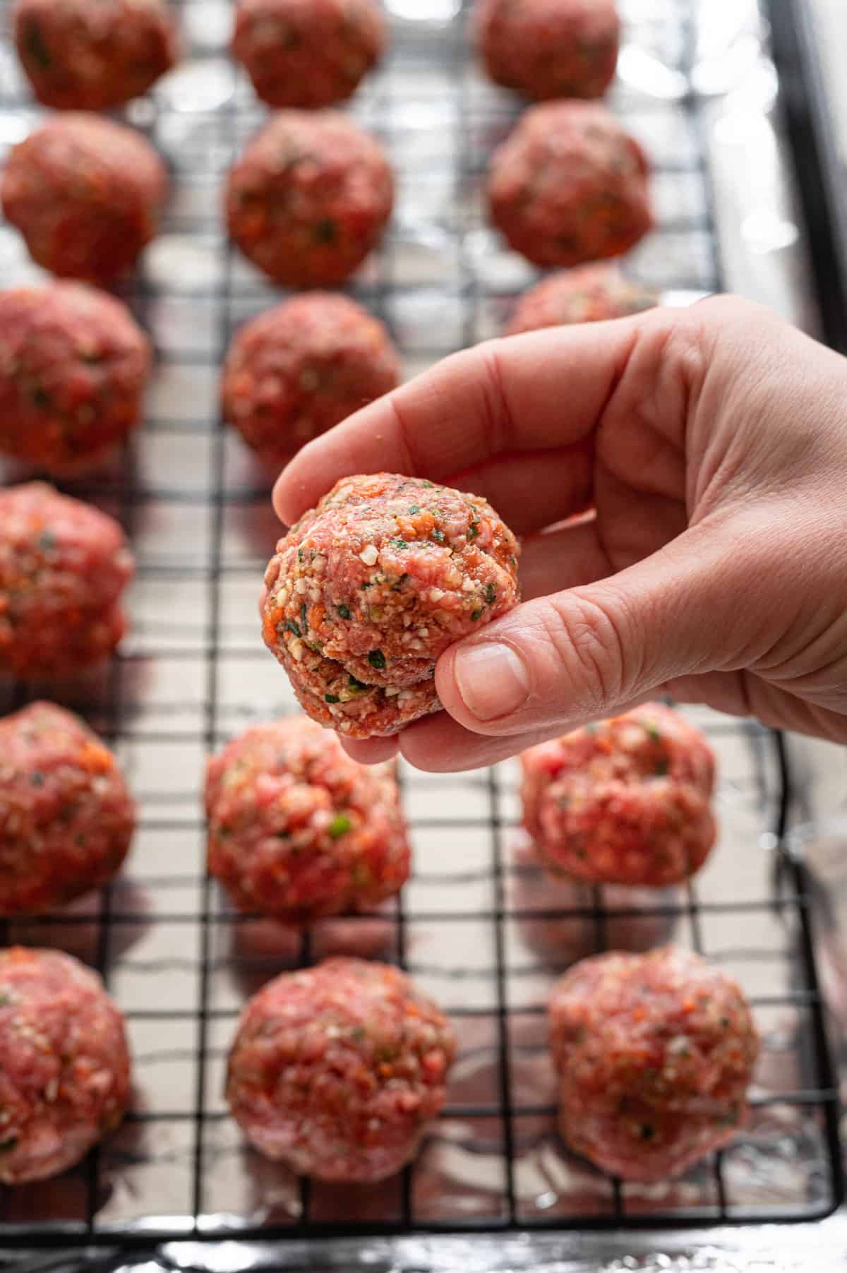 Meatballs on a rack on a foil-lined baking sheet with a hand holding one above the rest to show the size.