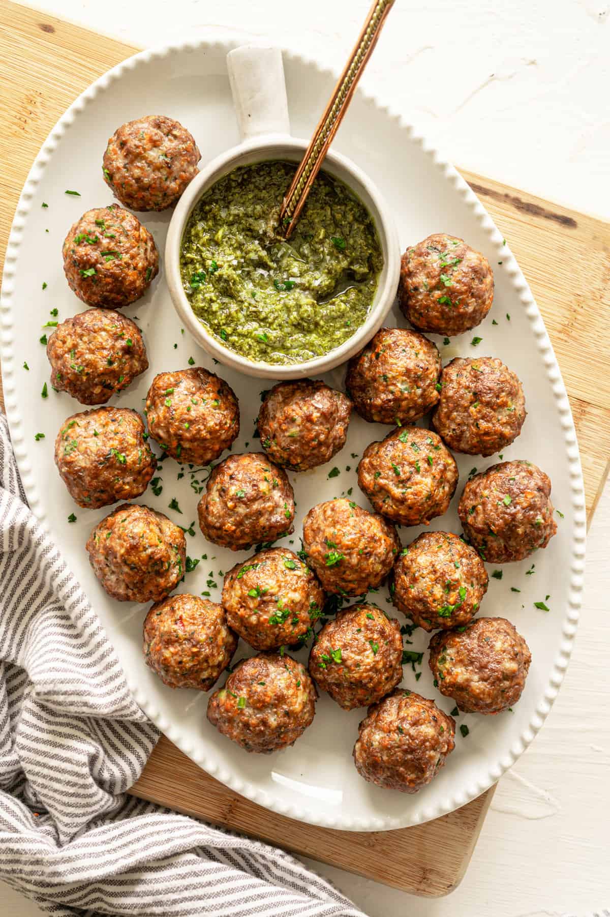 Baked healthy meatballs on a platter with pesto in a small bowl.