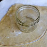 Whole wheat pastry dough rolled out and being measured to cut with a mini mason jar.
