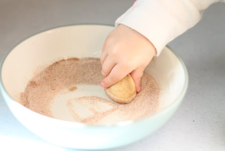 Toddler hand rolling cookie dough in cinnamon and sugar.