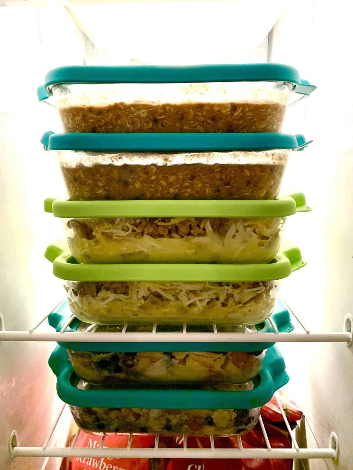 A stack of freezer meals in glass dishes with lids in a freezer.