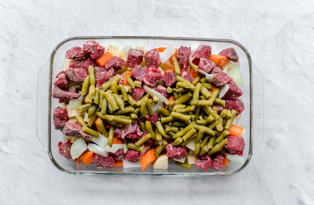 Uncooked Beef Stew in a casserole dish with stew meat, onions, carrots, green beans