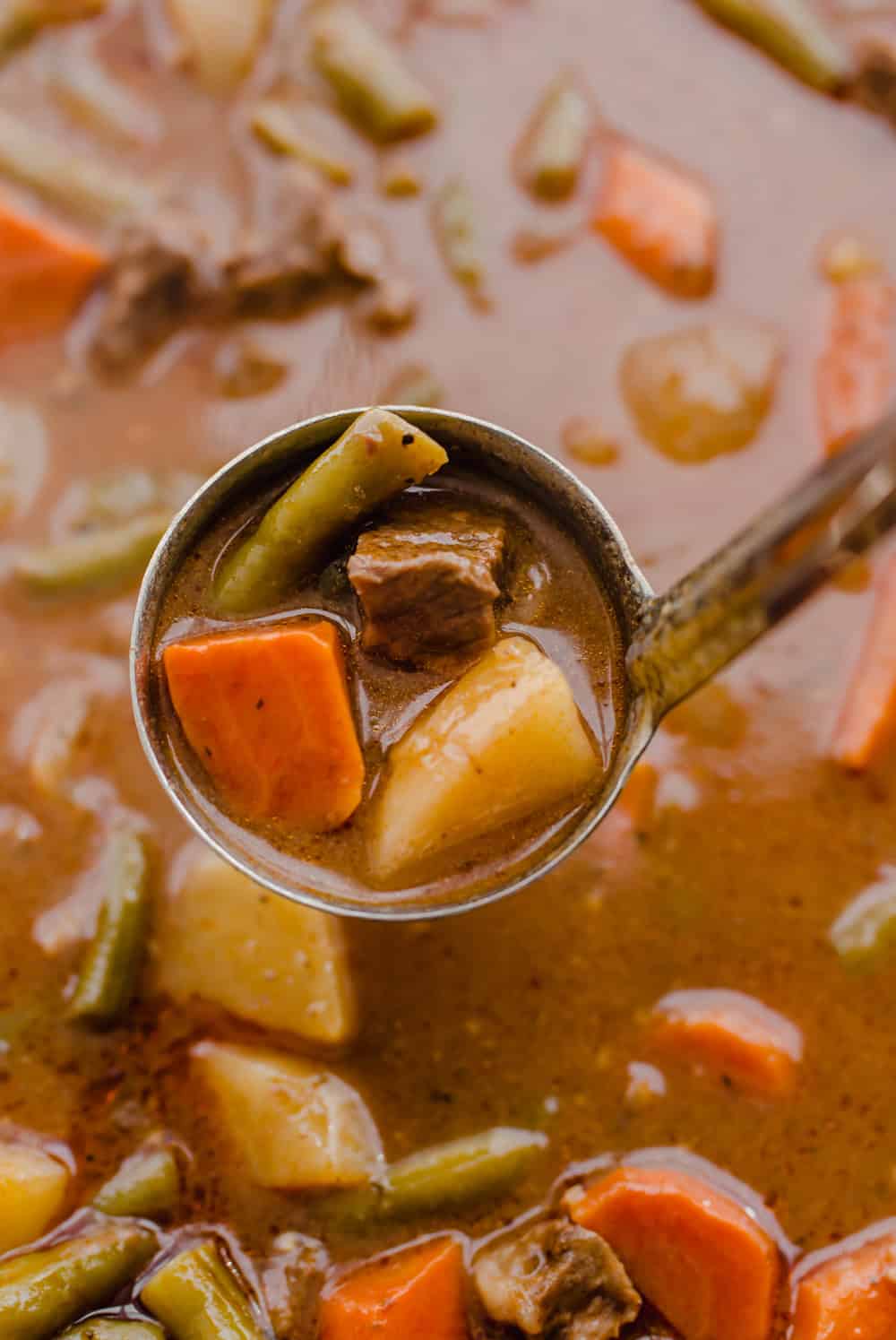 Ladle of easy beef stew with potatoes, carrots, onions, green beans, and stew meat.