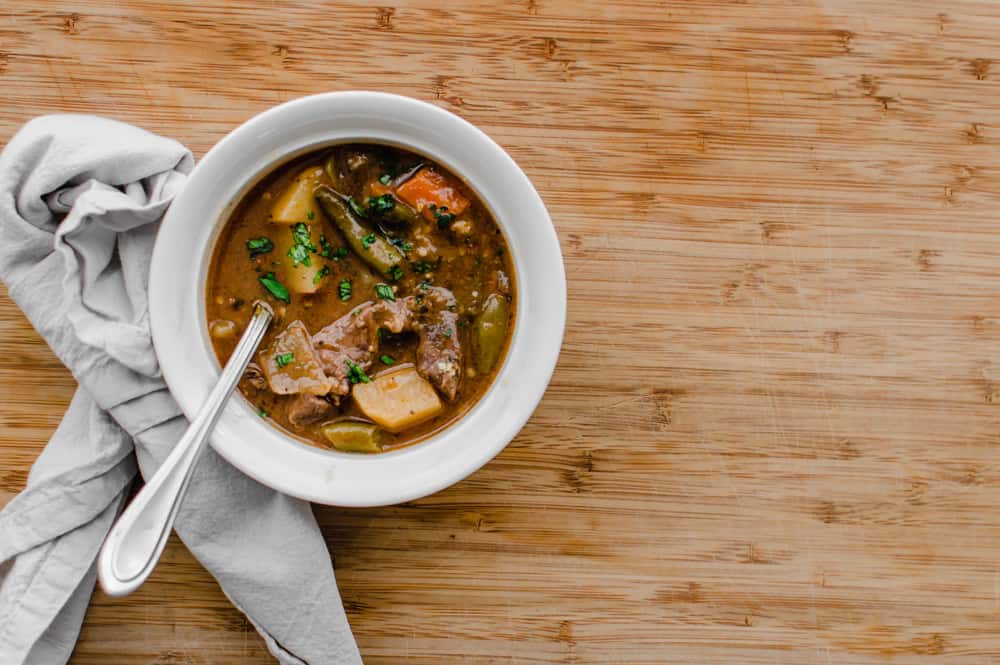 A bowl of easy beef stew with potatoes, carrots, onions, green beans, and stew meat in it. On a wooden table.