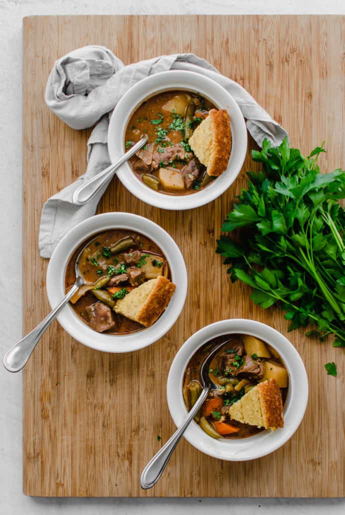 Bowls of easy beef stew with potatoes, carrots, onions, green beans, and stew meat in it. On a wooden table.