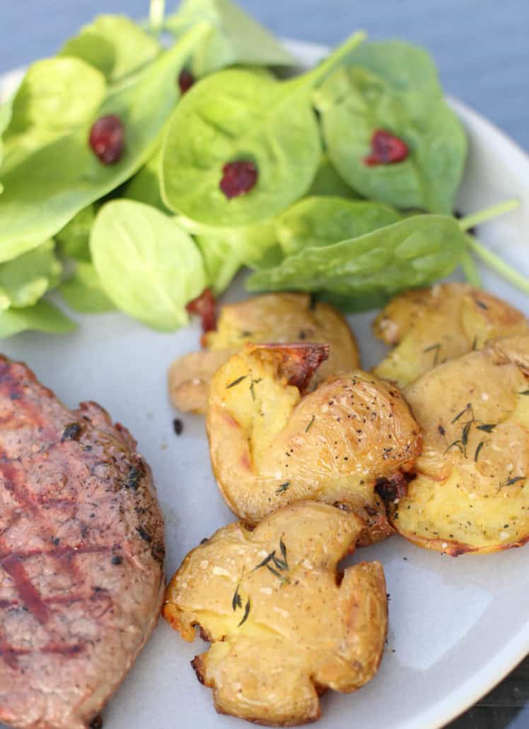 Crispy smashed potatoes on a plate with salad and steak