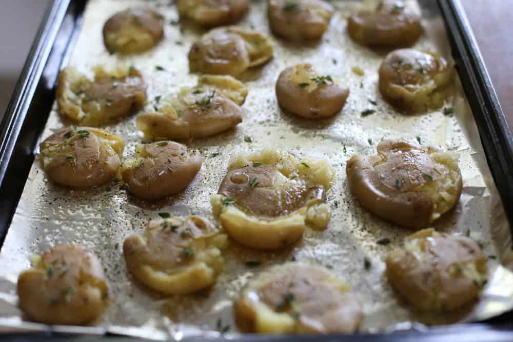 Smashed yukon potatoes on a foil-lined baking sheet seasoned and ready for the oven.