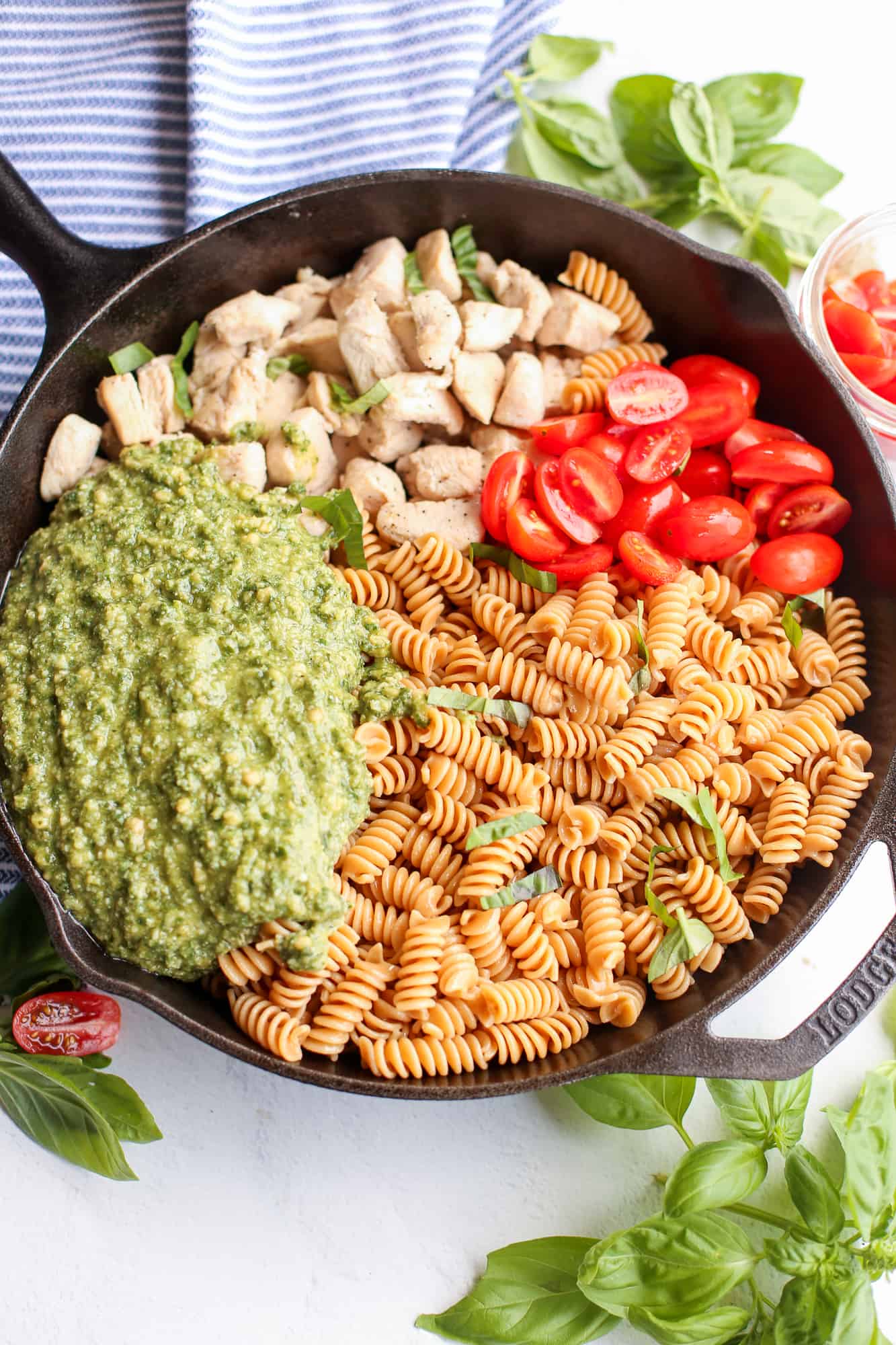Ingredients of chicken pesto pasta piled up in a skillet.