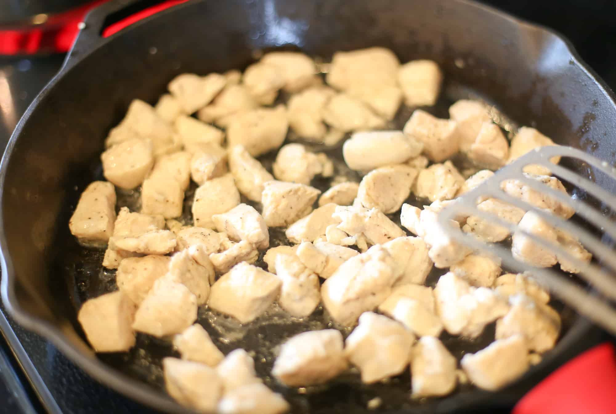 Diced chicken being sauteed in a cast iron skillet.
