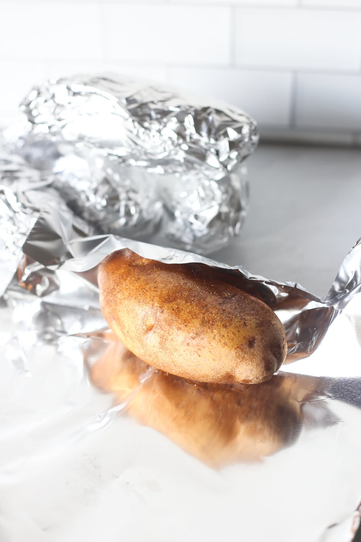 A russet potato being wrapped in foil.
