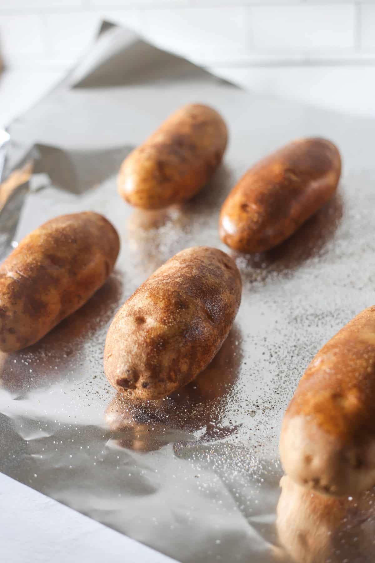 Russet potatoes lined up on a sheet of foil sprayed with oil and seasoned with salt and pepper. 