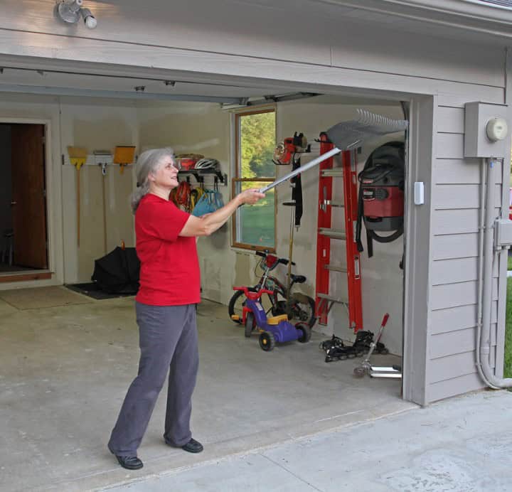 A woman holding a rake horizontally just outside her garage door as a hummingbird flies away.