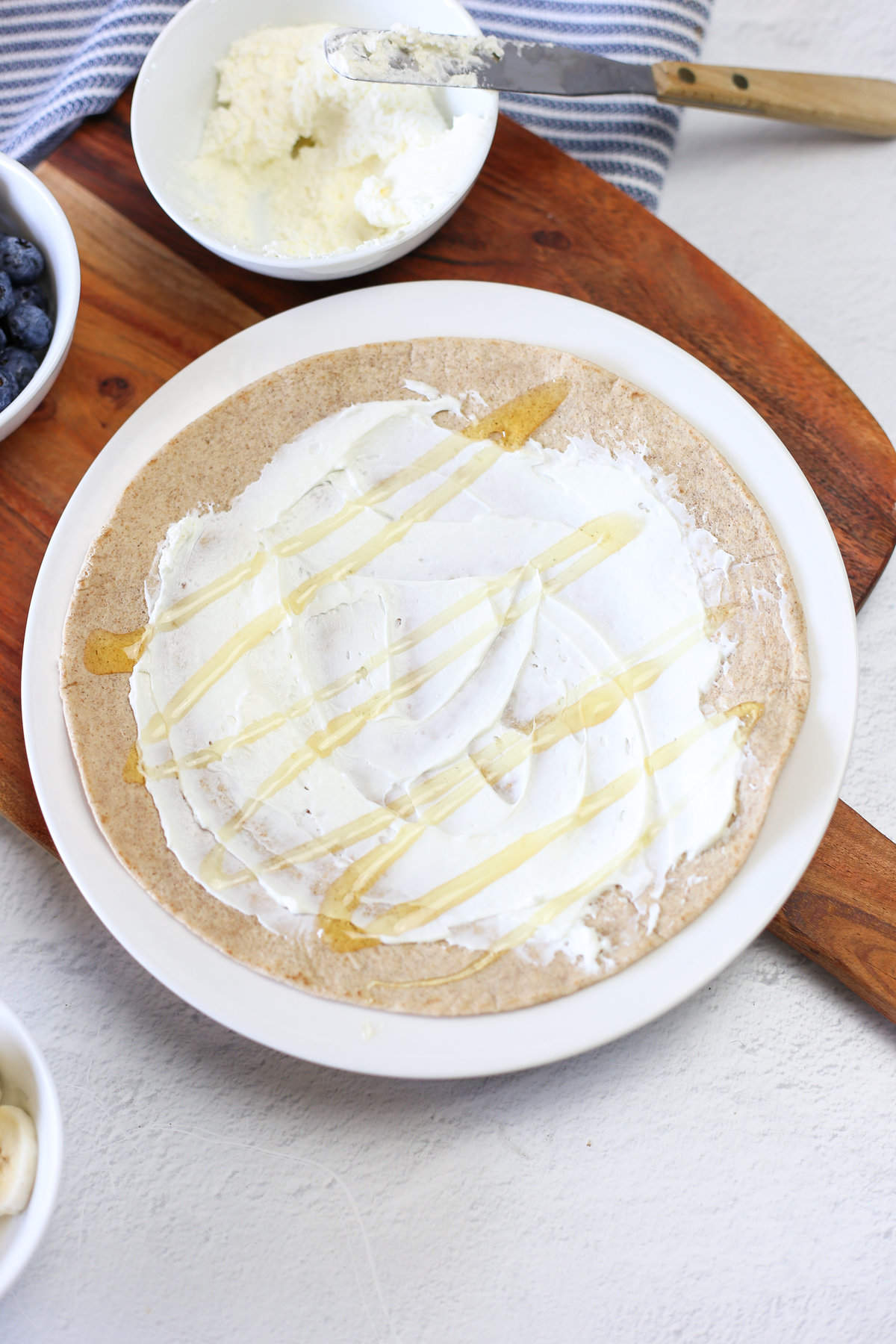 A drizzle of honey spread over a tortilla with cream cheese on it. 