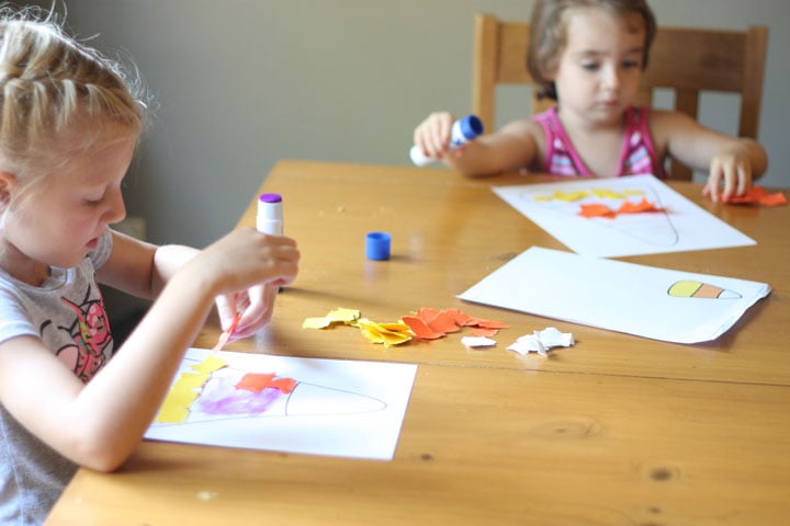 Two kids making a candy corn craft at a kitchen table.
