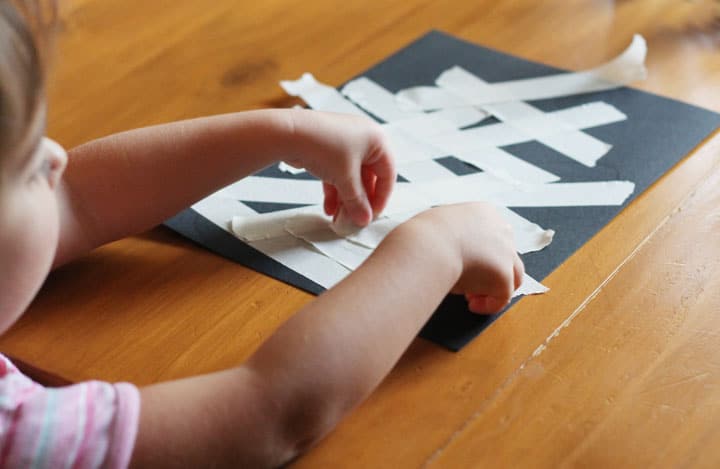 A child putting masking tape on a black piece of construction paper.