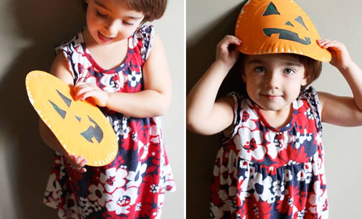 A little girl holding a completed paper plate pumpkin craft.