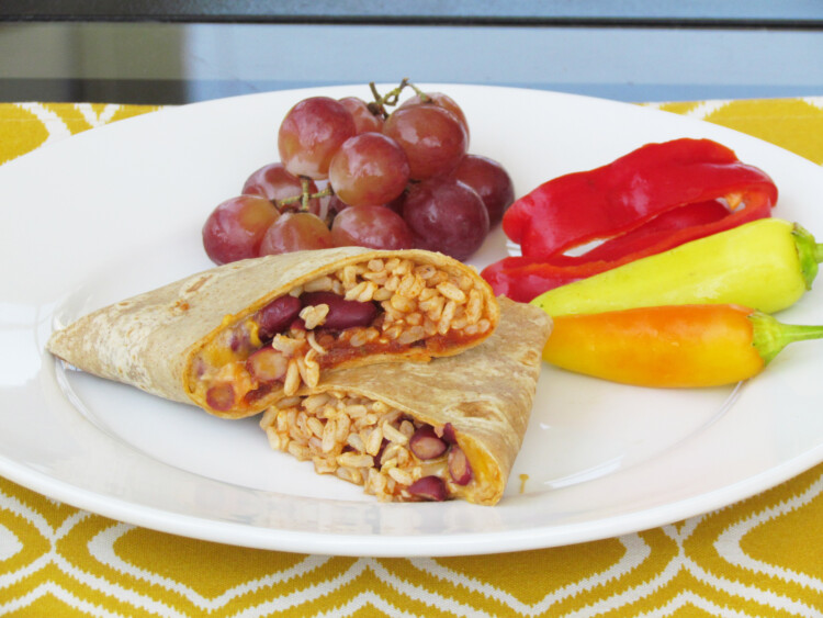 A lunch wrap cut in half with grapes and fresh cut veggies.