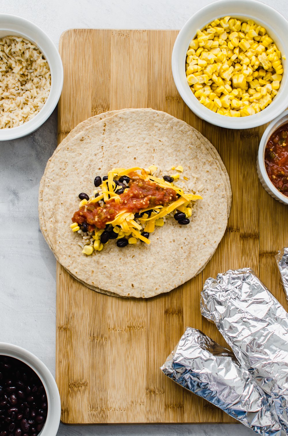 vegetarian lunch wraps on a wooden cutting board with small bowls of corn, salsa, and rice.