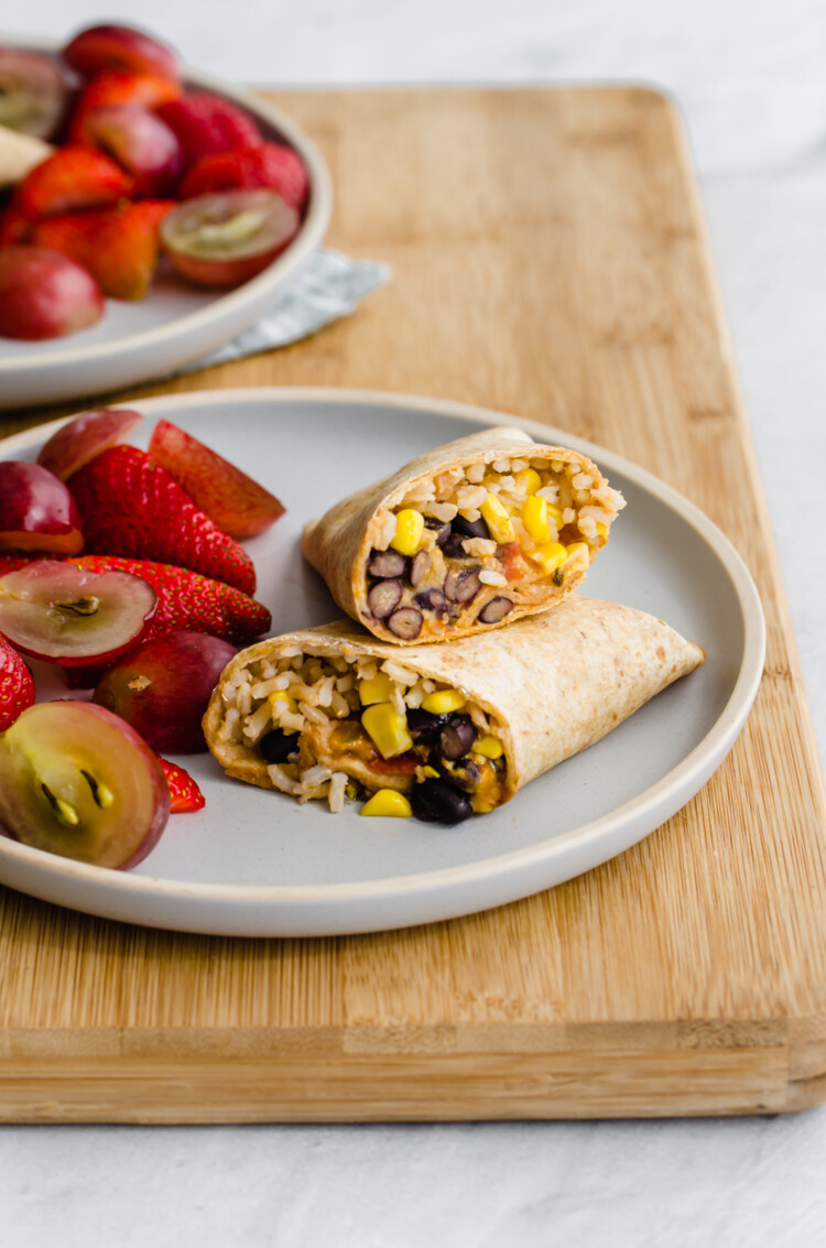 Freezer-friendly lunch wrap cut in half on a plate with fresh fruit.