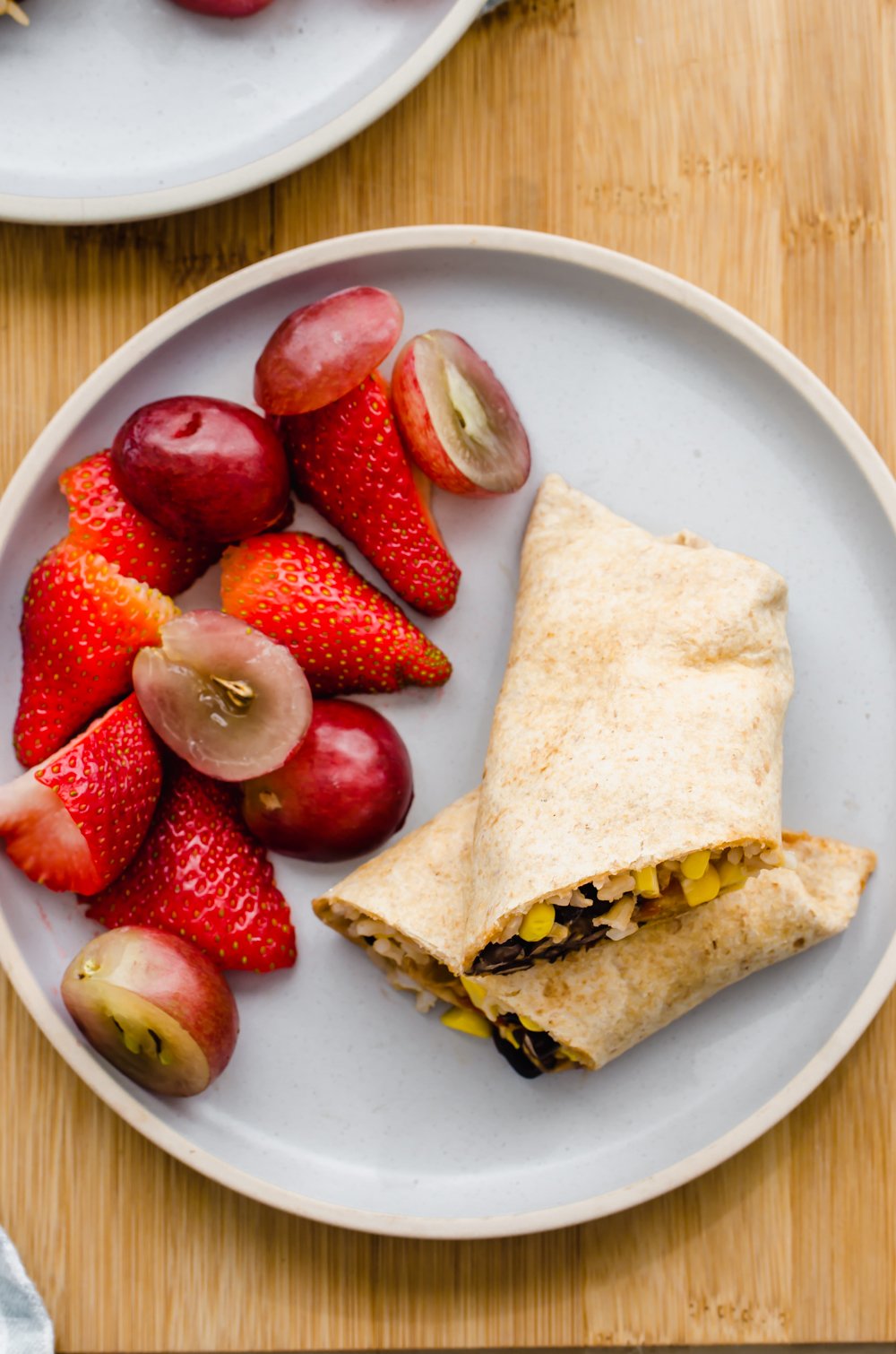 A lunch wrap cut in half with strawberries and grapes on a plate.