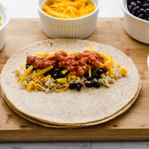 vegetarian lunch wraps on a wooden cutting board with small bowls of corn, salsa, and rice