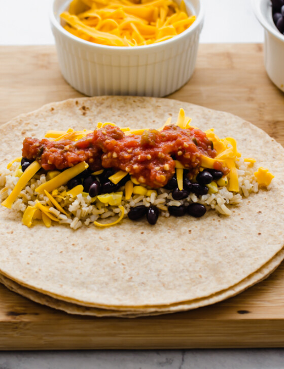 vegetarian lunch wraps on a wooden cutting board with small bowls of corn, salsa, and rice