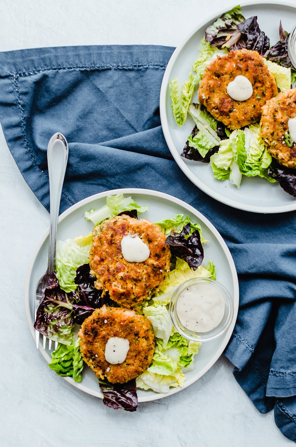 Salmon and sweet potato cakes on a bed of lettuce with avocado aioli being served on two plates.