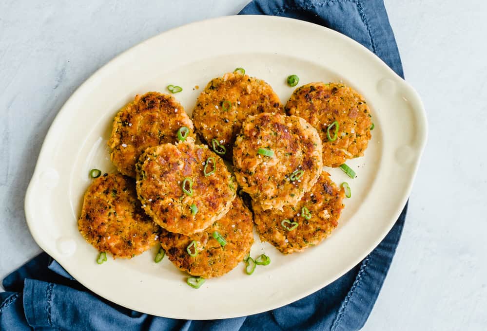 Salmon and sweet potato cakes lined up on a white serving platter.