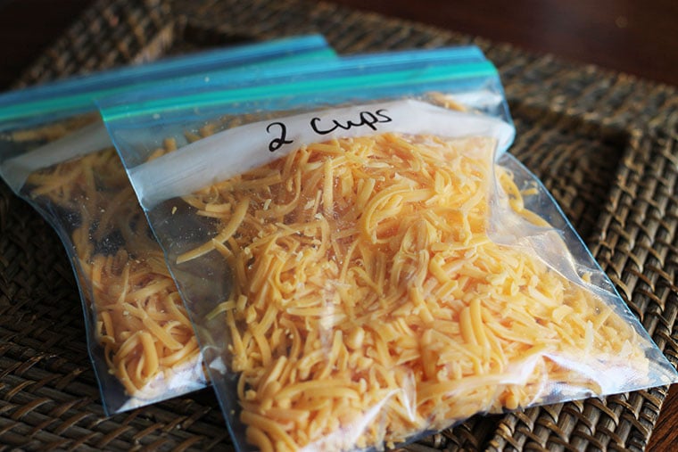 Two quart-size freezer bags filled  with freshly shredded cheddar cheese each labeled 2 cups.
