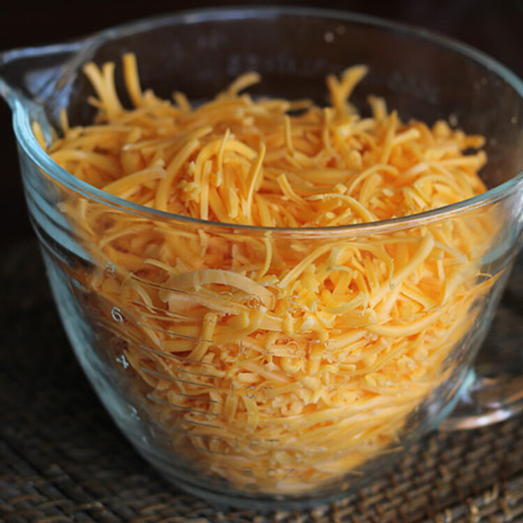 Cheese that was shredded with a grater into a glass mixing bowl.