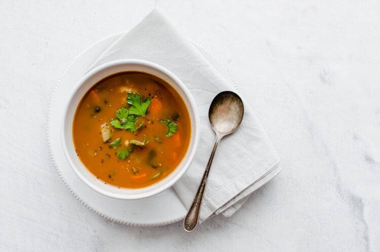 Bowl of vegetable soup in a white bowl with a spoon.