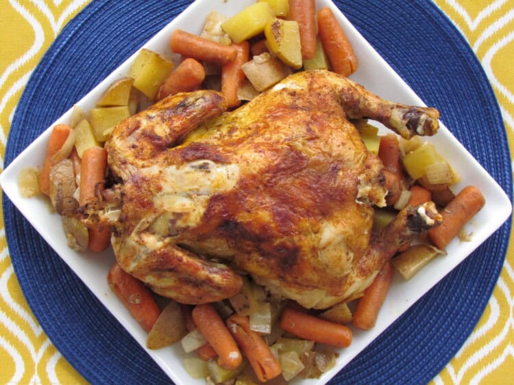 Whole chicken on top of cooked carrots and potatoes on a platter.