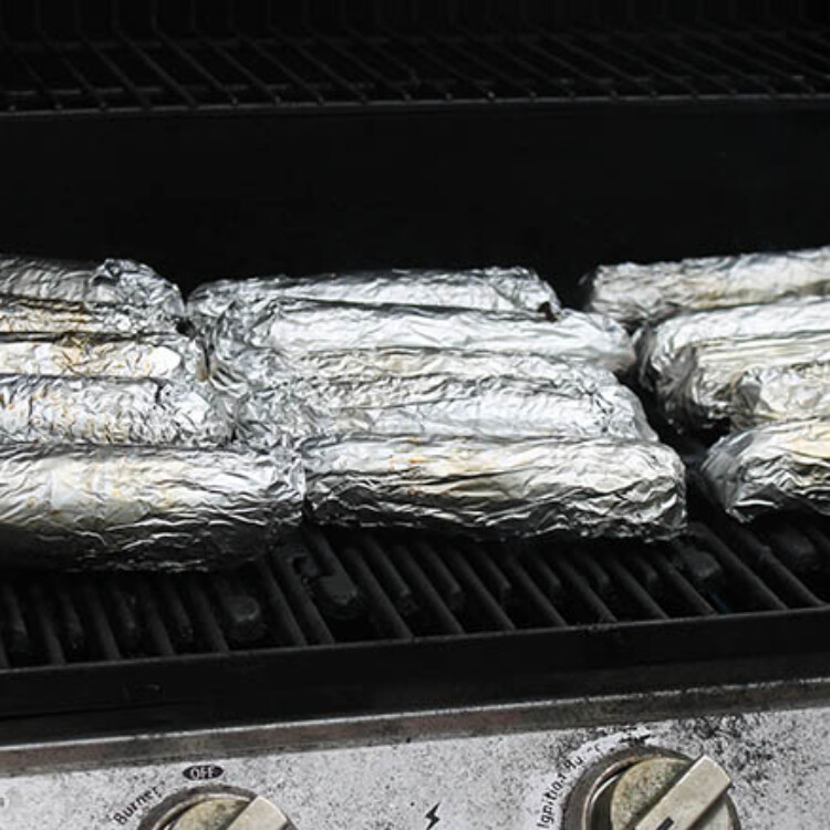 12 ears of corn wrapped in foil being grilled.