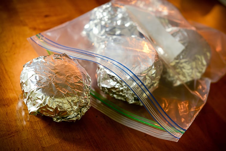 English muffin breakfast sandwiches wrapped in foil and being put into a freezer-safe baggie to be frozen.