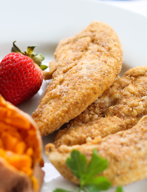 Baked Chicken Tenders on a plate with sweet potato and strawberries.