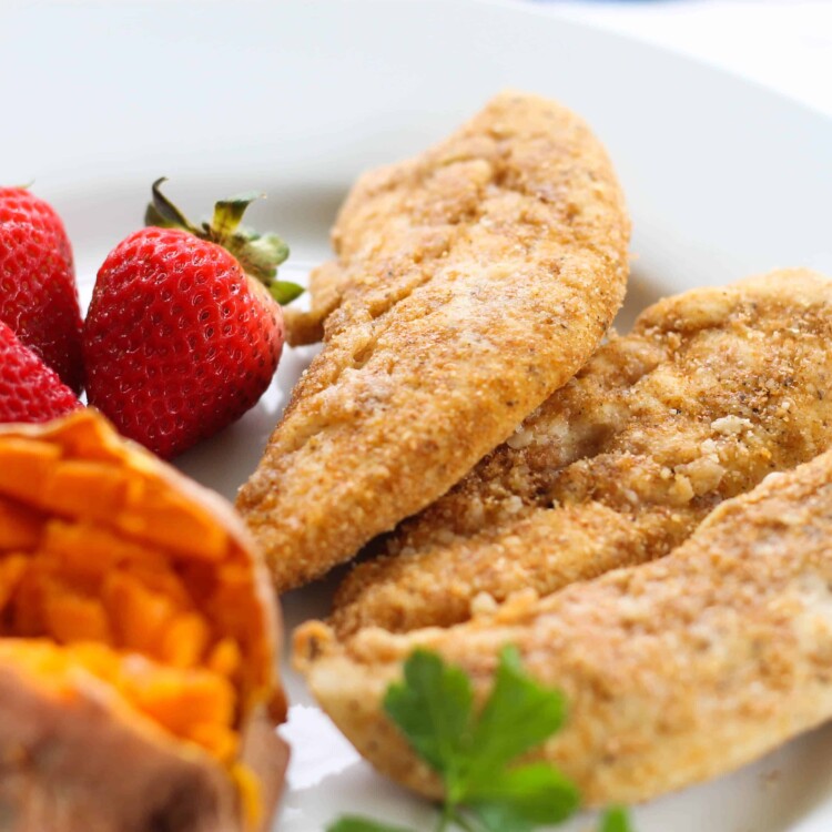 Baked Chicken Tenders on a plate with sweet potato and strawberries.