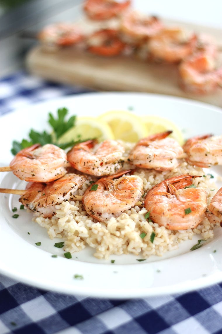 Mediterranean shrimp on skewers laying on a bed of rice with lemon wedges on the side.