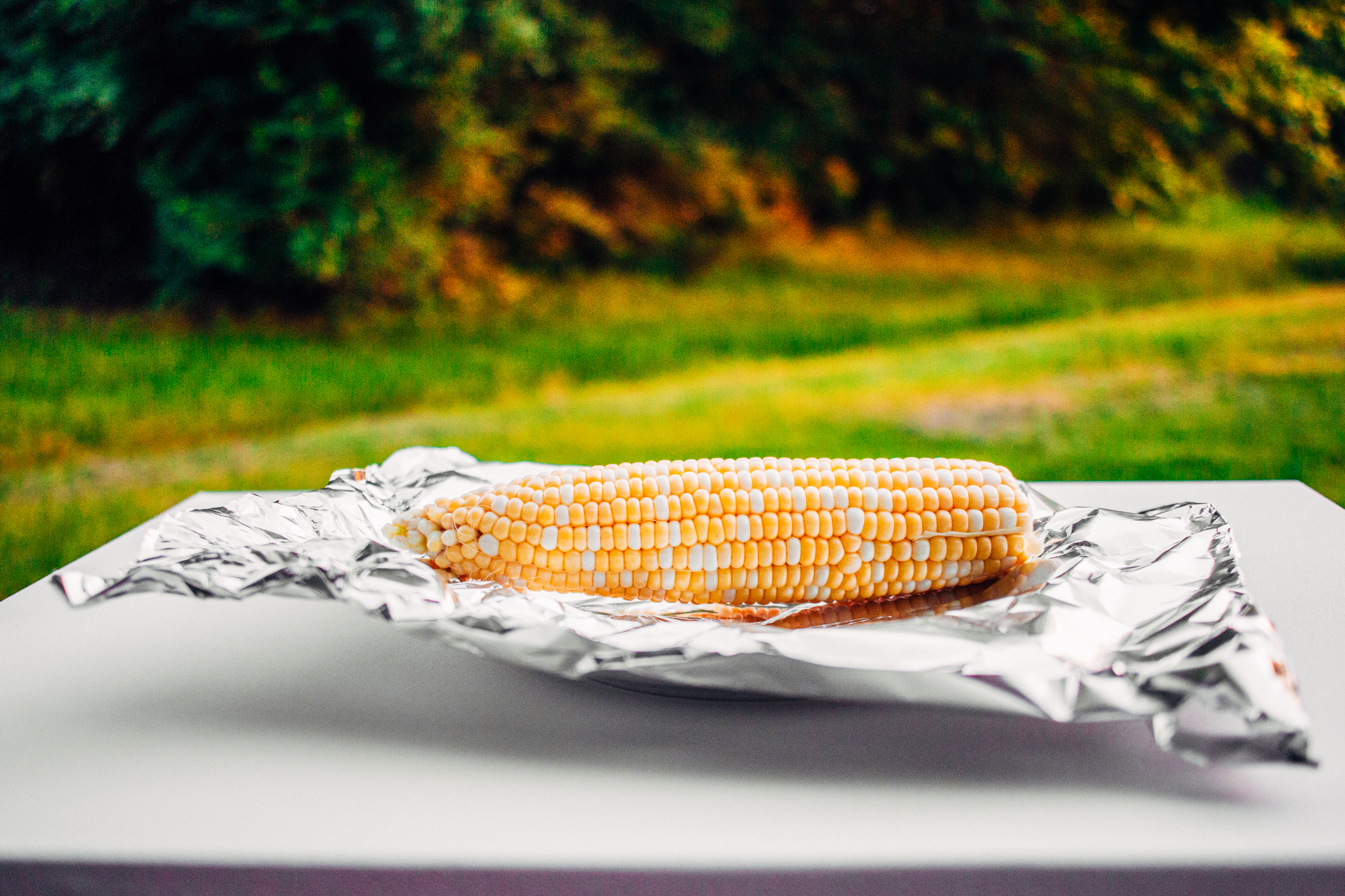 Corn on the cob sitting on a sheet of foil on a table outside.