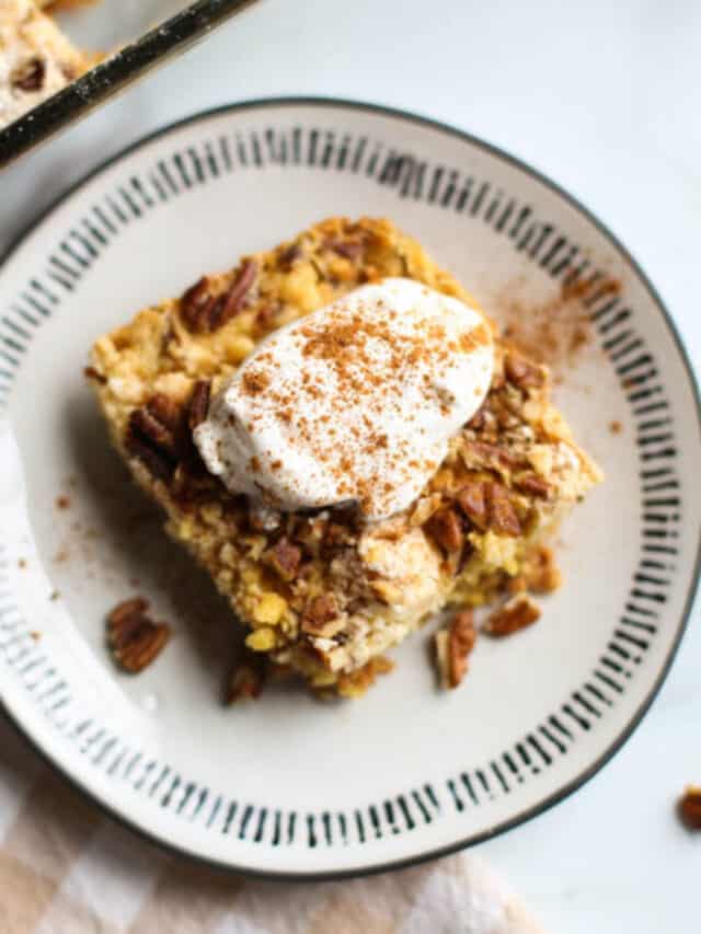 Slice of pumpkin dump cake on a plate with whip cream and a sprinkle of cinnamon on top.