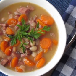 Ham and bean soup on a white bowl with fresh parsley on top.
