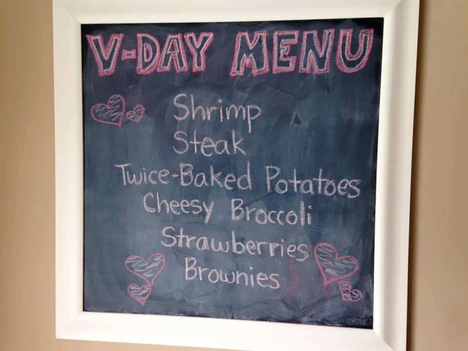 Valentine's day menu written on a chalkboard: Shrimp, Steak, Twice-Baked Potatoes, Cheesy Broccoli, Strawberries, Brownies.