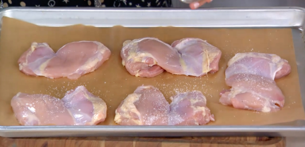 Chicken thighs on a baking sheet being seasoned