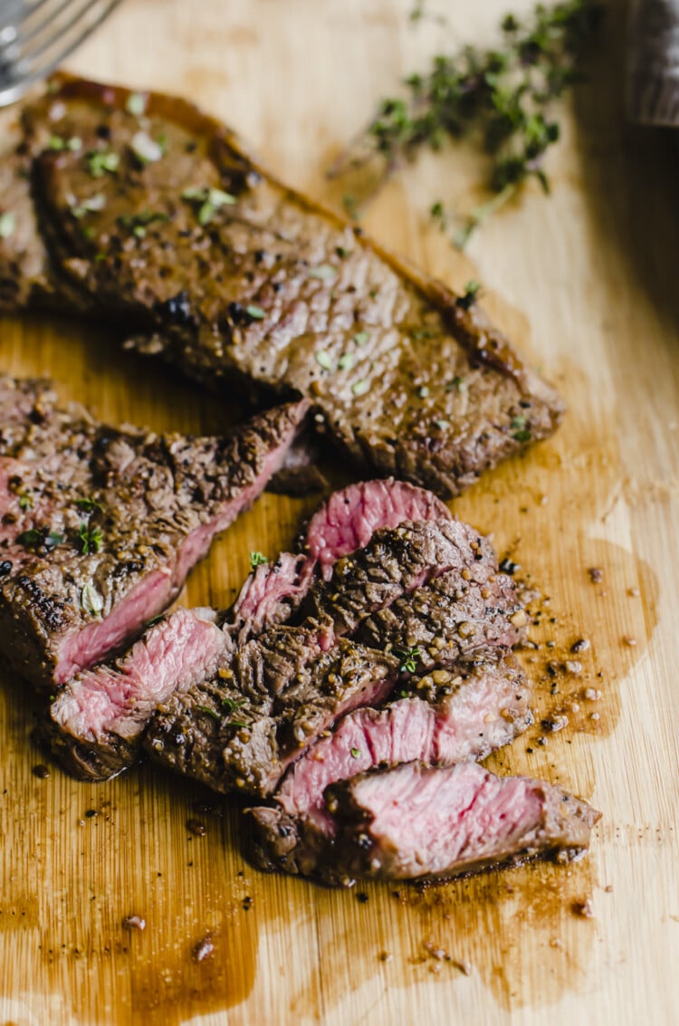seasoned cooked steak that is sliced on a wooden cutting board