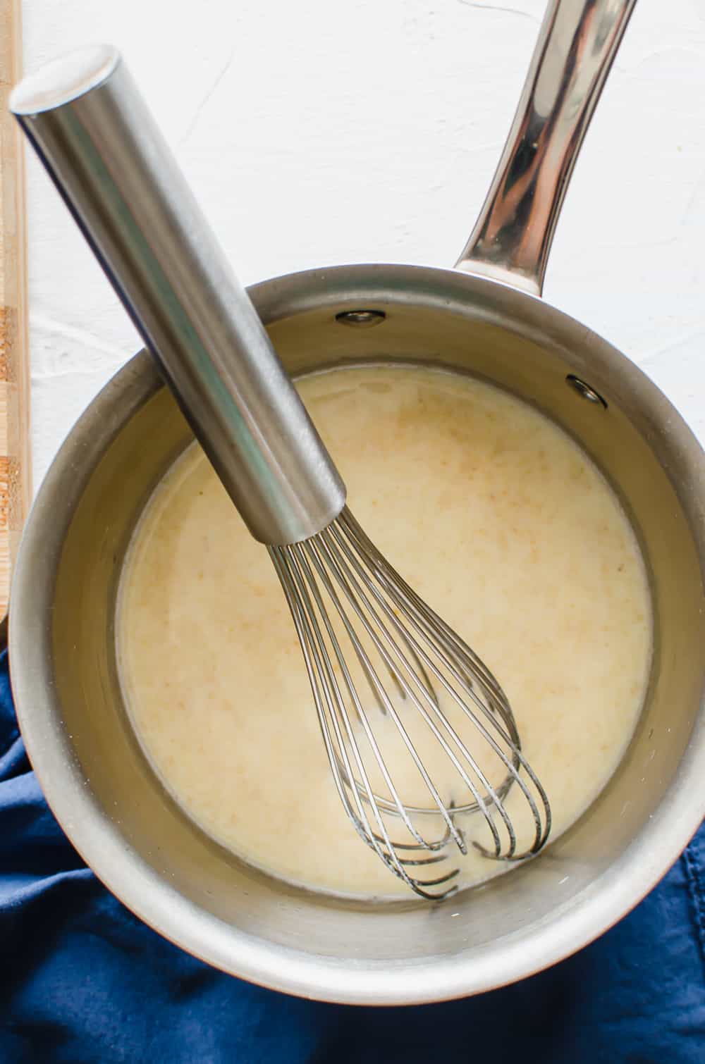 Milk added to a roux in a saucepan with a whisk.